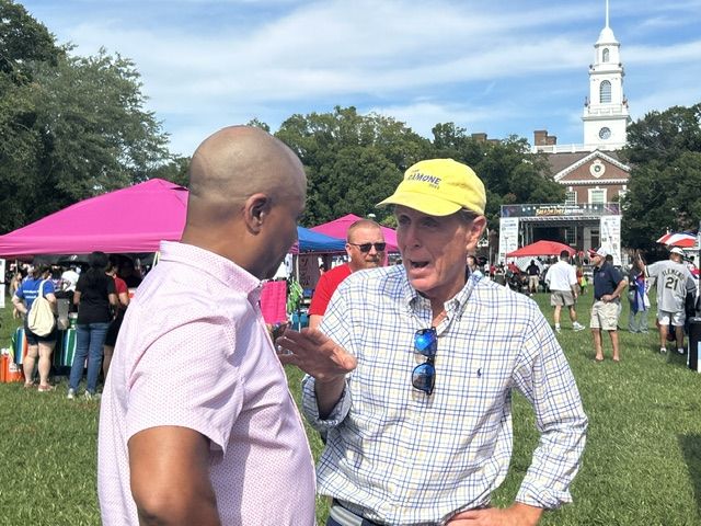 Mike Ramone in a yellow cap talking with a man among the festival tents.