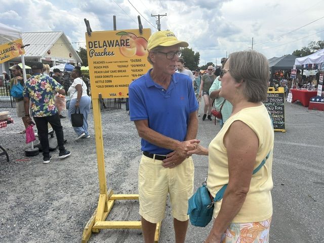 Mike Ramone talking with a woman beside the Delaware Peaches sign at the Wyoming Peach Festival.